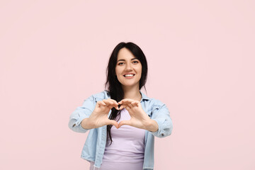 Happy young woman making heart with her hands on pink background