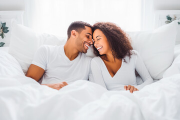 Fototapeta premium Beautiful young couple smiling and laying in bed with white sheets