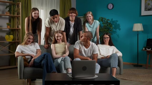 Full-size video of a group of teens, young people gathered around a laptop to speak, talk with, have a video call with their friend, friends, chatting joyfully.
