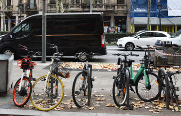 Bicycle parking on city street in Barcelona. City bikes at rental site. Bicycles for rental. Rent bike parked. Cycle station. Сity street, road traffic, cars on road and buildings. Broken bike parking