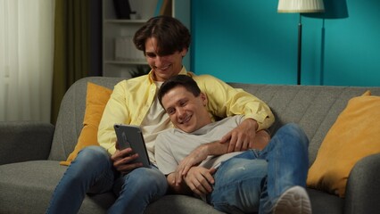 Shot of a homosexual couple at home. They are laying on the couch, watching photos or videos on a...