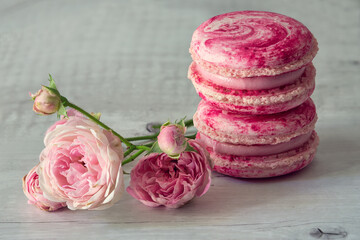 French macarons with rose flavor and fresh rose flowers on a wooden background