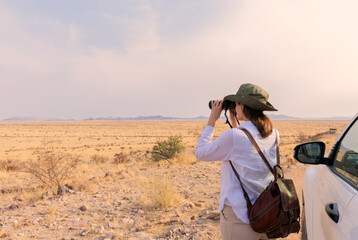 Woman with binoculars enjoying a beautiful view of the African savannah during a safari tour in Tanzania and Kenya. Adventure and wildlife exploration in Africa. Serengeti National Park. © xamnex