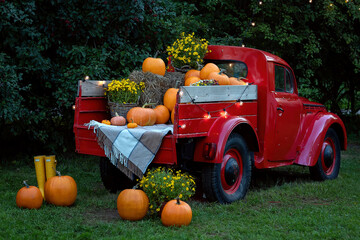 A vintage red old truck filled season flowers hay and festive fall orange pumpkins.