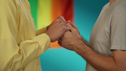Close up, detail shot of a homosexual, transgender, pansexual, bisexual, asexual male or non binary couple standing in front of each other, holding hands.