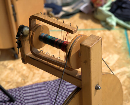 Close up of a wooden spinning wheel bobbin, in action with yarn passing through the small metal thread holders.