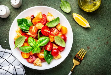 Panzanella vegetable salad with stale bread, colorful tomatoes, olive oil, sea salt and green basil, green stone table background, top view