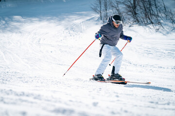 Confident skier skiing downhill in high mountains. Handsome, fashionable man in full sports equipment being photographed in movement on ski slope. Experienced male skier skiing in the mountains. - obrazy, fototapety, plakaty