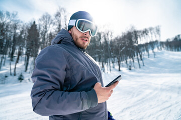 Portrait of male skier in gray jacket with mobile phone looking at camera. Close up photo of...