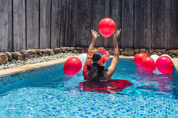 Jolie jeune femme habillée jouant avec des ballons rouge gonflable dans sa piscine de chambre d'hôtel