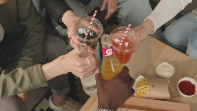 Top view slowmo of group of friends toasting with soft drinks while having fun at home eating pizza and celebrating