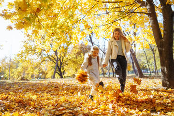 Little daughter and her mother with autumn yellow leaves have fun together in a city park in autumn. Childhood concept, walks, weekends.
