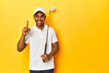 African American man golfer, yellow studio backdrop, showing number one with finger.