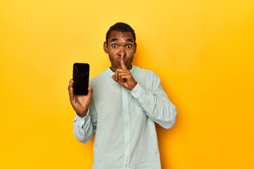 African American man with mobile phone, yellow studio, keeping a secret or asking for silence.