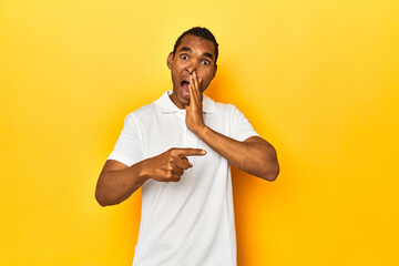 African American man in white polo, yellow studio, saying a gossip, pointing to side reporting...