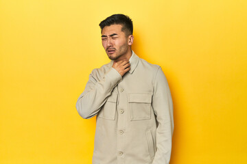 Fototapeta premium Asian man in stylish gray shirt on yellow studio suffers pain in throat due a virus or infection.