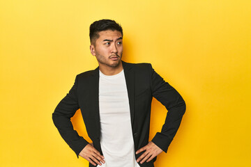 Asian man in black business jacket on yellow studio confused, feels doubtful and unsure.