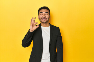 Asian man in black business jacket on yellow studio cheerful and confident showing ok gesture.