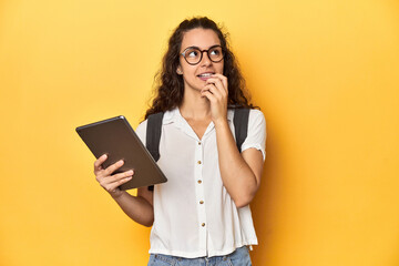 Student holding a tablet, glasses, backpack on, relaxed thinking about something looking at a copy space.