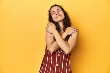 Young Caucasian woman, yellow studio background, hugs, smiling carefree and happy.