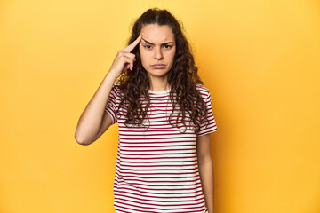 Fototapeta premium Young Caucasian woman, yellow studio background, pointing temple with finger, thinking, focused on a task.