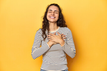 Young Caucasian woman, yellow studio background, laughing keeping hands on heart, concept of happiness.