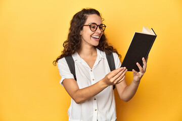 Young Caucasian woman engrossed in reading a book in a studio with yellow backdrop.