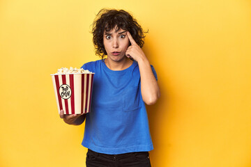 Curly-haired woman with popcorn for movie, studio showing a disappointment gesture with forefinger.