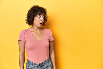 Curly-haired Caucasian woman in pink t-shirt being shocked because of something she has seen.