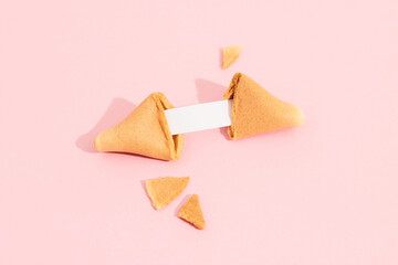 Fortune cookie on a pink background with deep long shadow. Blank paper for prediction words