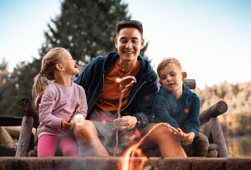father spending time with his children having fun roasting marshmallows over a campfire having fun...