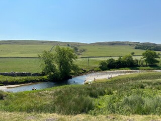 View across the, River Wharfe, with wild grasses, dry stone walls, people, and distant hills near, Kilnsey, UK