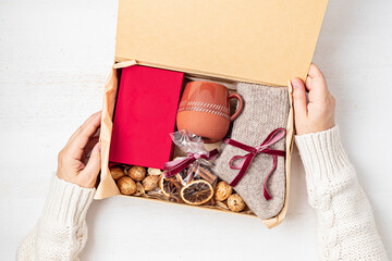 Preparing care package with warm socks, book, coffee cup, aroma spices. Personalized eco friendly...