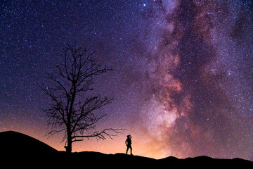 Fantasy landscape, silhouette of a hiker standing on the hill, on the milky way galaxy background.