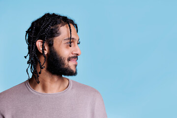 Smiling arab handsome man with braided hair looking to left side. Young adult attractive person with positive facial expression posing for profile studio shot on blue background