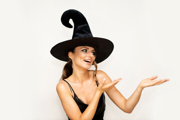 A young woman in a black witch's hat in a black silk dress and with bright evening makeup points to something on the right next to her