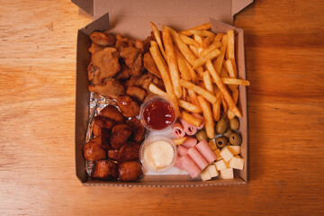 Overhead view of a box of assorted snacks with toppings on a wooden table.