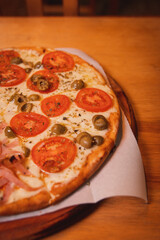 Detail shot of a pizza with tomato and olives on a wooden table.