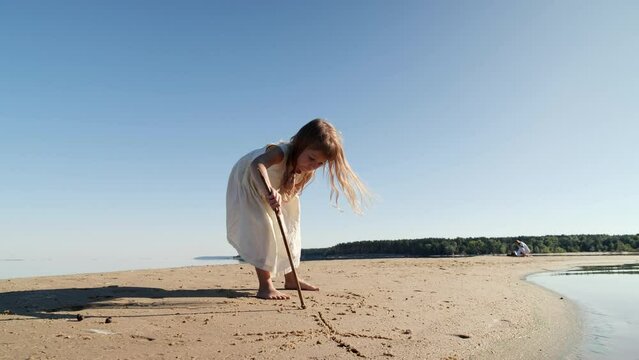 Girl child drawing with a stick on the sand on the beach and having fun