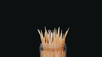 Wooden Toothpicks Rotate on a Black Background. Close up. A set of bamboo toothpicks in a transparent plastic cup. Home oral care after meals. Teeth cleaning. Blurred motion. Dentistry concept. Loop. - Powered by Adobe