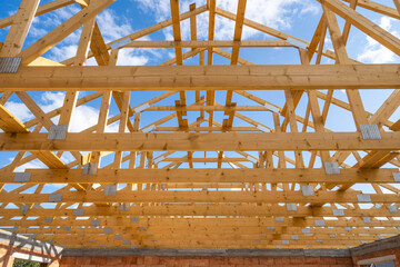 Frame of new house with wooden roof without coating against blue sky on background - obrazy, fototapety, plakaty