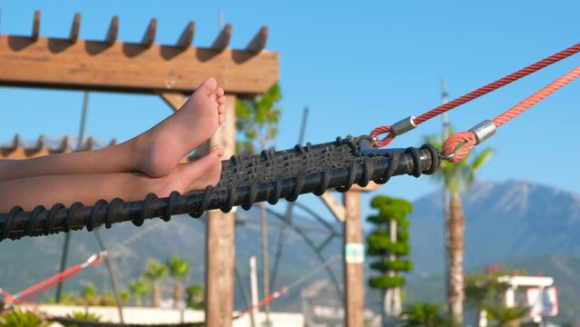 Child legs in hammock by trees. A sunny hammock with child legs relaxing in it against park trees in summer.