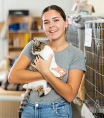 Happy caring young girl holding curious white and gray cat in arms while visiting shelter for abandoned animals. Pet adoption concept