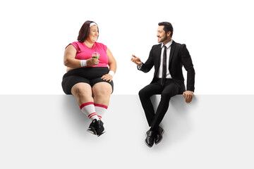 Obraz premium Businessman talking to a corpulent woman seated on a blank panel and holding a healthy green smoothie