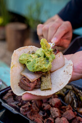 person making a delicious Mexican style carne asada taco with avocado and salsa.