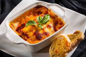 Italian lasagna on a white square plate with fresh basil leaves
