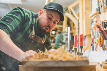 Portrait of carpenter blowing off wood shavings from workstation. High quality photo