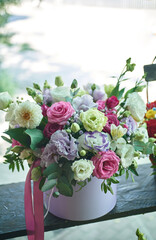 Bouquet of flowers in a white box with pink ribbon, inside a florist's shop. Roses, peonies and others in shades of pink, white and purple.
