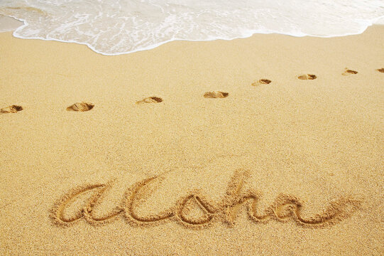 Aloha Written In Sand With Footprints And Wave Wash.