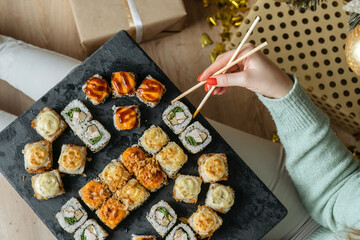 Sushi sticks in the hands of a woman against a set of sushi on a slate. Oriental cuisine.